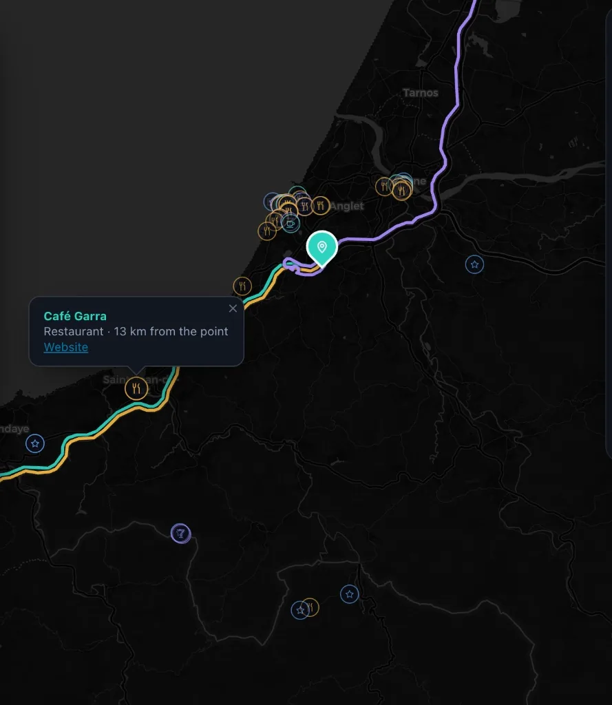 The map zoomed in on the Basque coast: three coloured routes running side by side into the meeting pin, glyph chips for nearby places, and a popup for Caf&eacute; Garra.